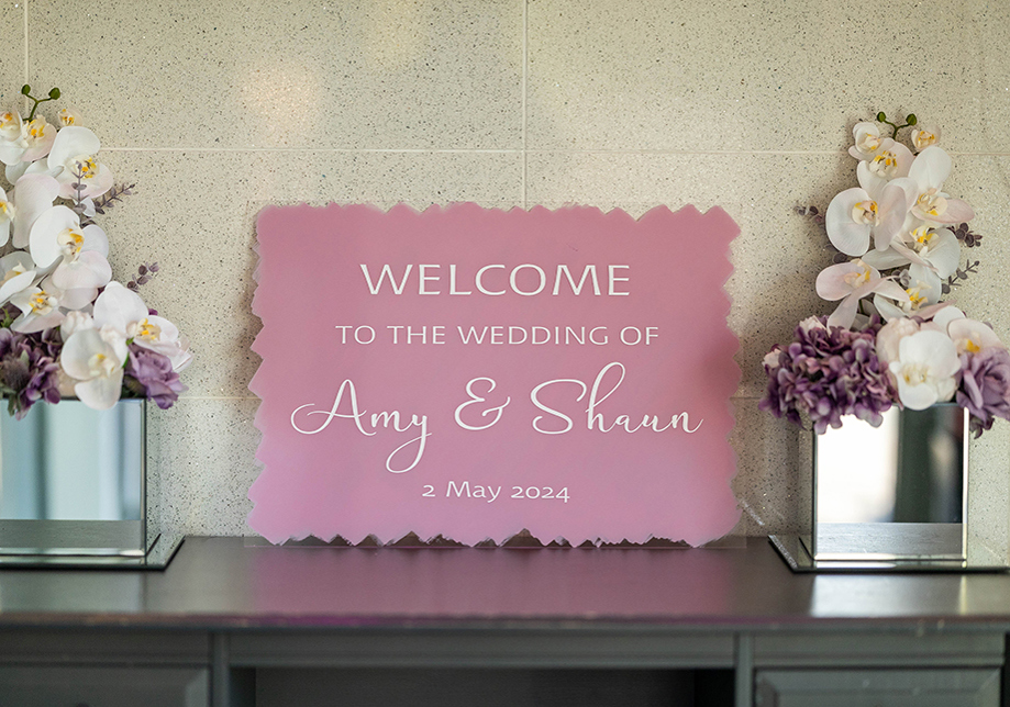 Pink welcome sign beside two plants in square mirrored plantpots